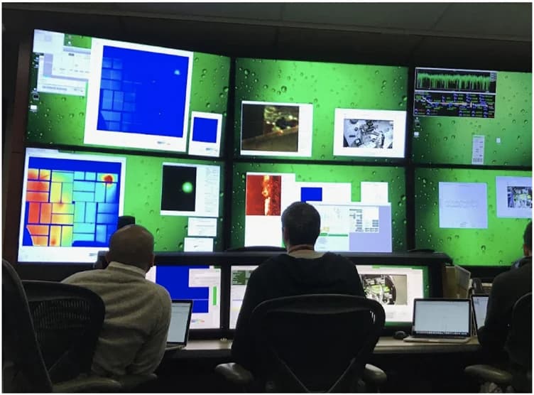 Instrument operators working in a control room with multiple experimental data displays.